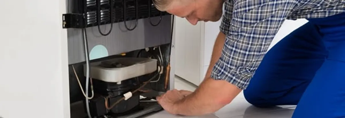 Refrigerator repair technician servicing the compressor and condenser area in Stockton, CA